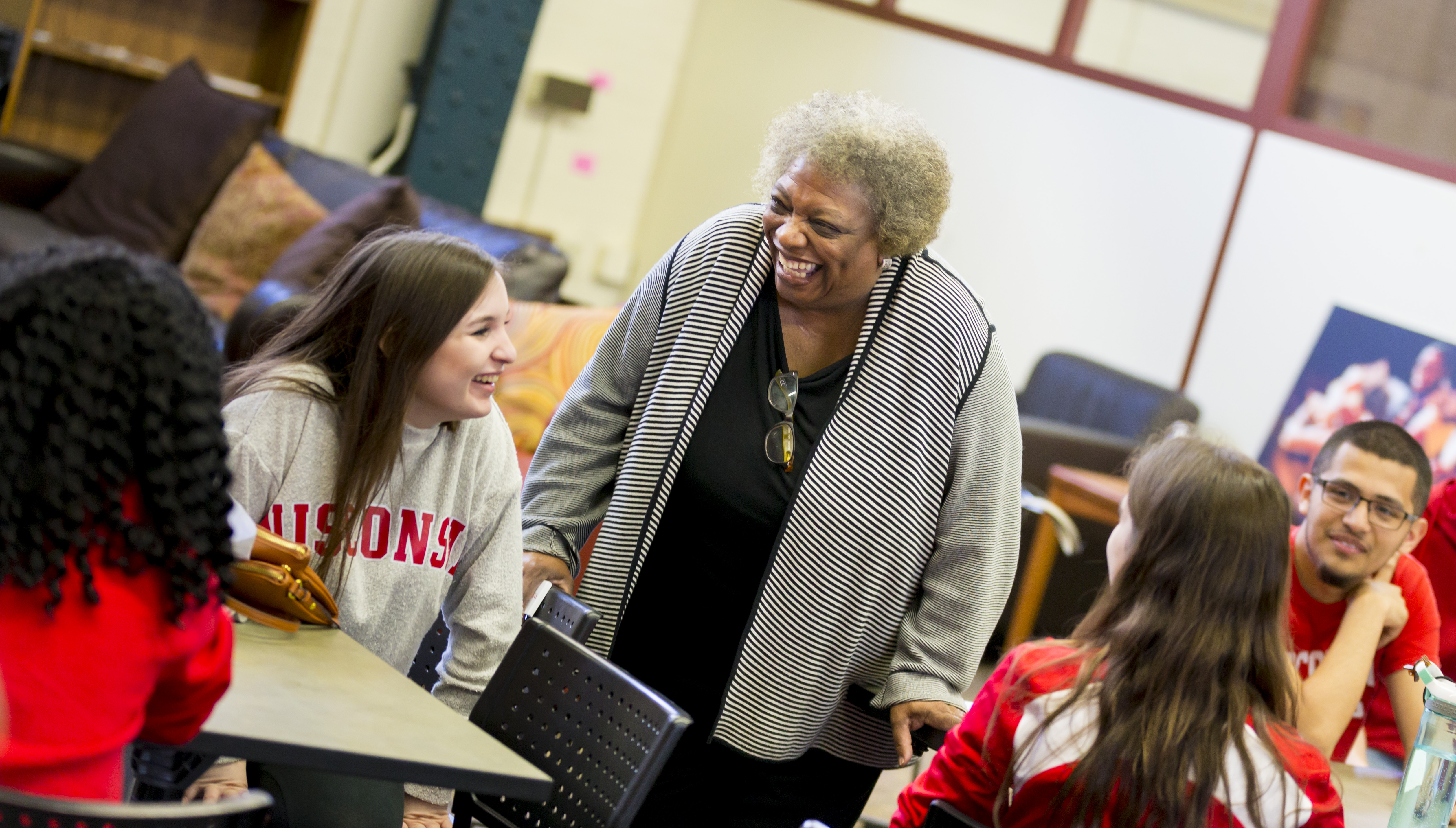 Former director Gloria Hawkins stands in the middle of four scholars seated at tables.