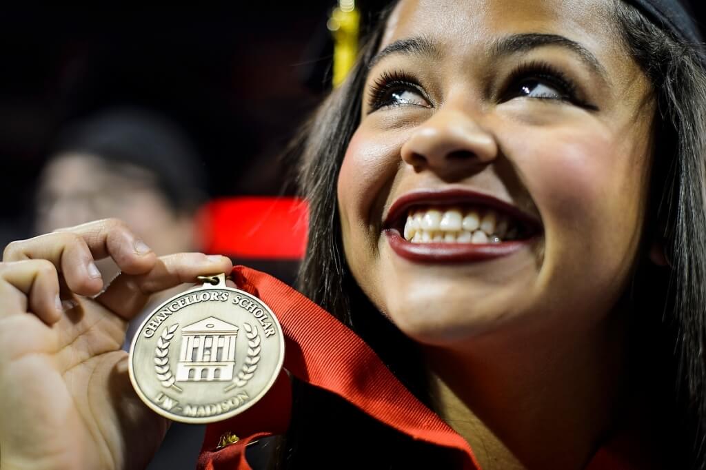 A female graduating scholar holds her medallion which is embossed with Mercile J Lee Scholars Program.