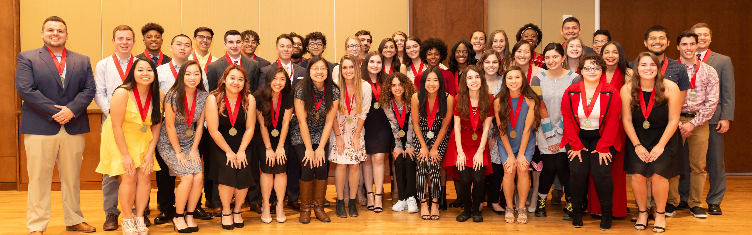 A large group of students all wearing gold medallions on red sashes around their necks pose for a group photo.