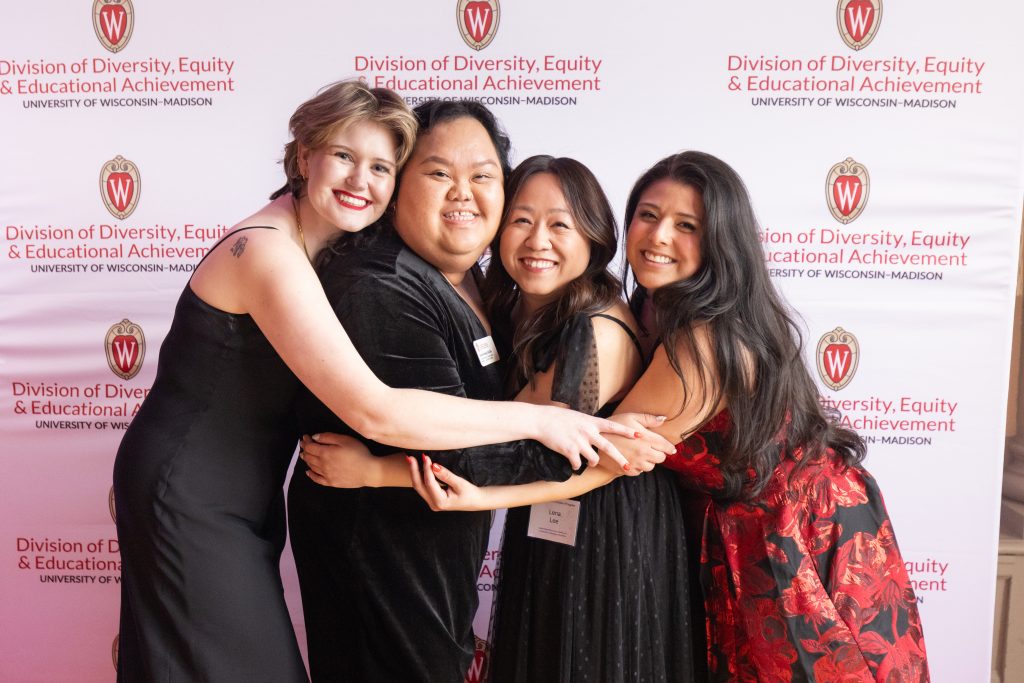 Mercile J. Lee staff members posing wearing cocktail gowns in front of a DDEEA backdrop.