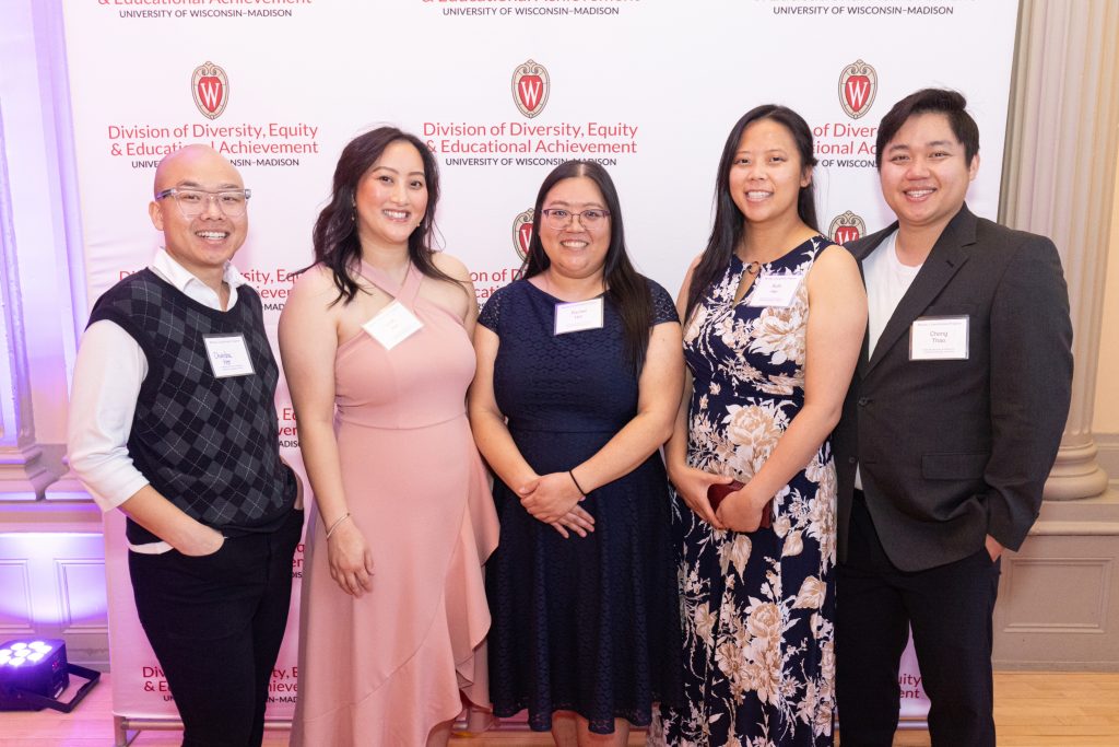 Picture of 5 people in formal attire smiling in front of a backdrop