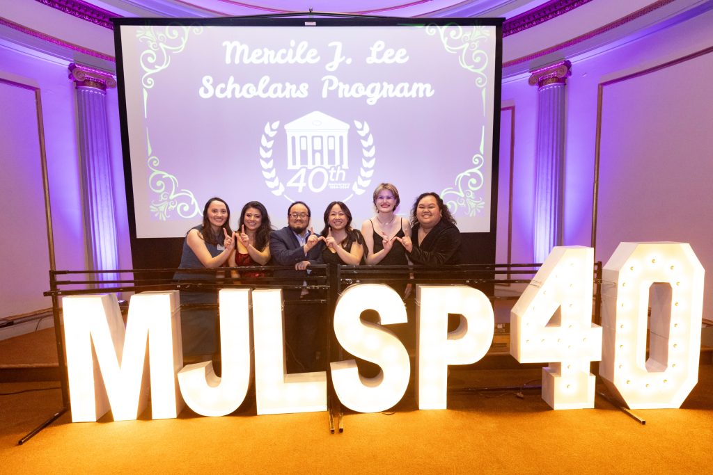 Mercile J. Lee Scholars Program staff members smiling behind a neon MJLSP light in a purple backlit room.