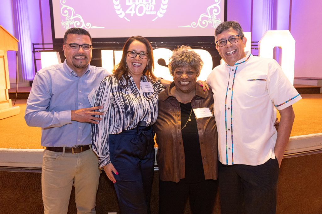Picture of 4 people smiling in front of a stage