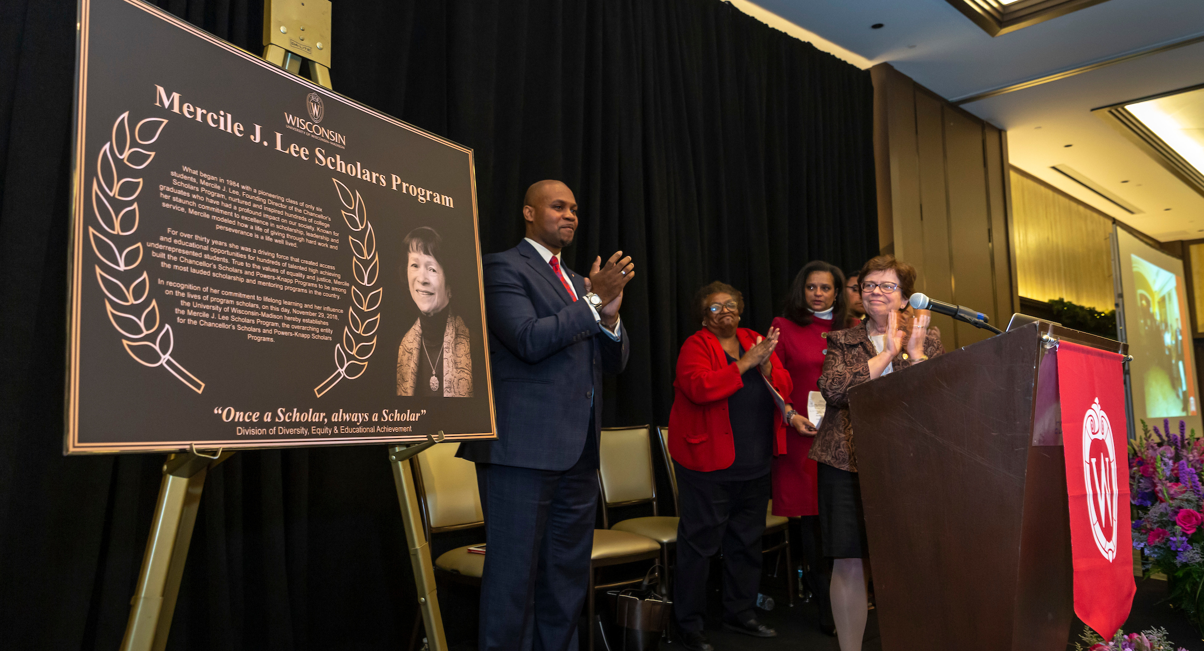 Administrators clapping behind a podium as Mercile J. Lee Scholars Program plaque is unveiled.